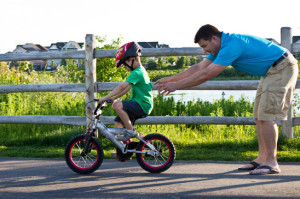Child learning to ride a bicycle with father