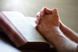 Hands folded in prayer on a Holy Bible in church concept for faith, spirtuality and religion