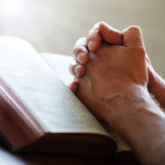 Hands folded in prayer on a Holy Bible in church concept for faith, spirtuality and religion