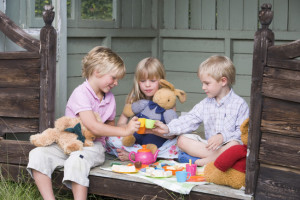 Three young children in shed playing tea and smiling